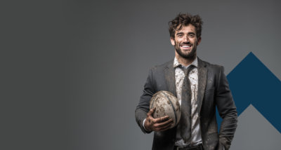 A photo of a muddy businessman holding a rugby ball and smiling